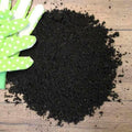 A pile of Soil Improver Conditioner sits on a wooden surface next to green gardening gloves with white polka dots.