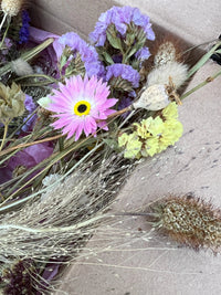 The Dried Flower Craft Box by Bishy Barnabees Cottage Garden features a close-up of pink daisy, purple and yellow blooms, beige seed pods, and wheat-like grasses—beautifully arranged in a brown cardboard box.