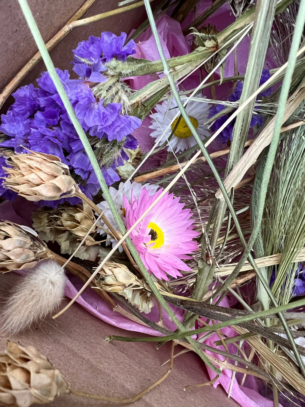 A close-up of Bishy Barnabees Cottage Garden's Dried Flower Craft Box shows a bouquet with purple, white, and pink dried flowers plus grasses on pink tissue—ideal for your next craft project or use as dried flowers for crafts.