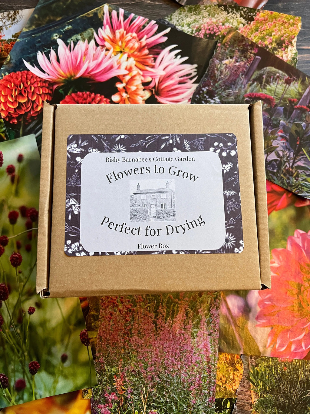 A brown box labeled "Flowers Perfect for Drying Extra" from Bishy Barnabees Cottage Garden sits atop floral photos, featuring a cottage illustration and offering seeds ideal for growing flowers to create lasting dried bouquets.