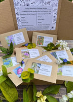 A selection of "Flowers to Grow...Perfect for Pollinators" seed packets by Bishy Barnabees Cottage Garden, attractively arranged with fresh leaves and flowers on wood—ideal for bringing pollinators to your garden.