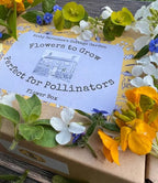 The Flowers to Grow...Perfect for Pollinators box by Bishy Barnabees Cottage Garden features bee-friendly flowers in yellow, orange, blue, and white on its design, displayed on a wooden surface.