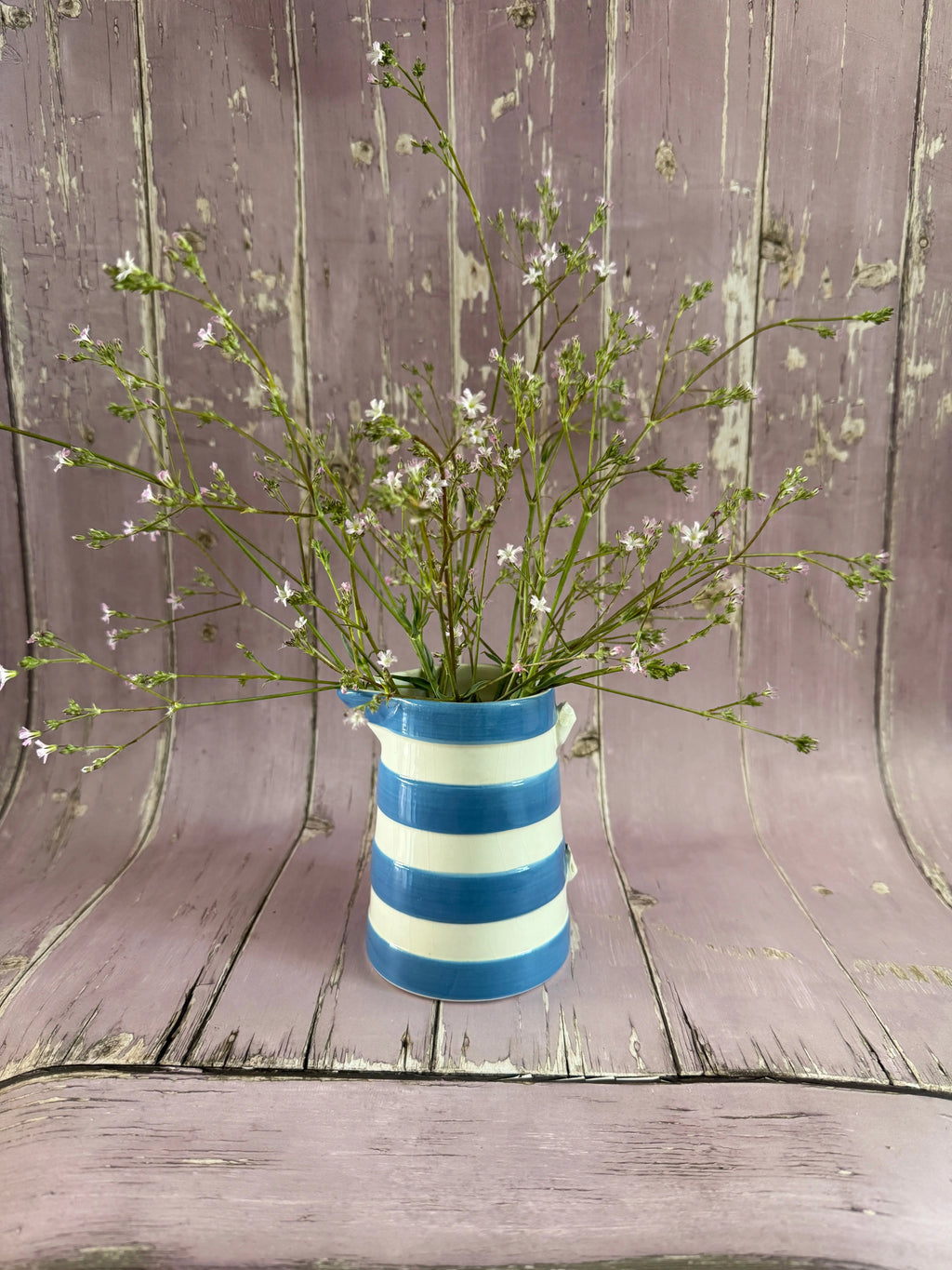 Gypsophila Pink in a blue and white striped vase against weathered pink wood