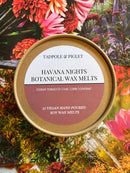 A round tin of Tadpole & Piglet’s Havana Nights Botanical Wax Melts sits on vibrant floral backdrops. This vegan, soy-based, hand-poured fragrance blends Cuban tobacco, oak, lime, and cognac for a unisex home scent experience.
