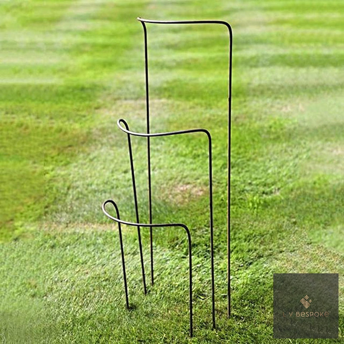 Set of metal half-hoop plant supports standing on a striped lawn