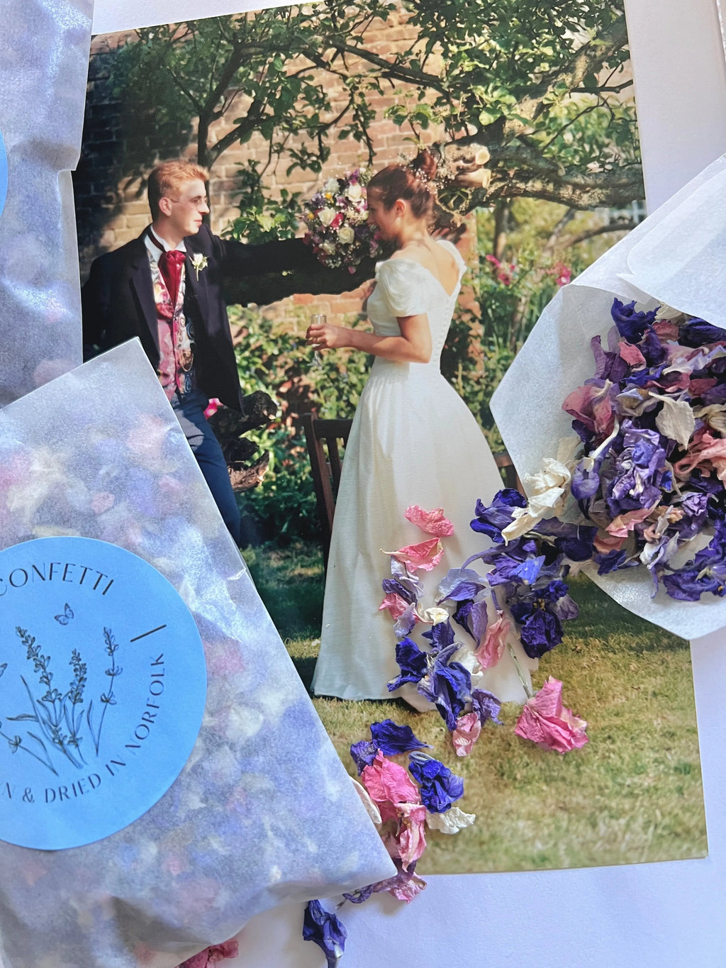 Larkspur Confetti in pink and purple spilling from blue packets over a wedding photo