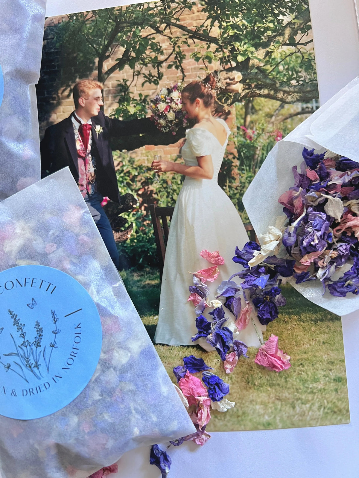Larkspur Confetti in pink and purple spilling from blue packets over a wedding photo