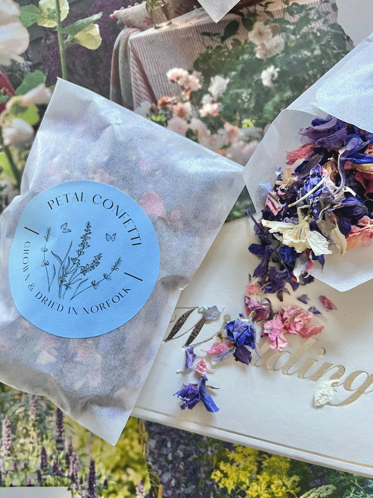 Larkspur Confetti 4g packet on a floral background with petals over a Wedding card