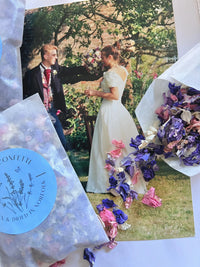 A bride and groom smile outdoors with a bouquet, as Bishy Barnabees Cottage Garden's Larkspur Confetti (Mixed Colours) 4g—biodegradable petals in pink and purple—spills from blue packets across the photo.