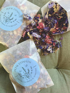Two 4g bags of Larkspur Confetti on green fabric with petals spilling out