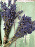 Two bundles of Bishy Barnabees Cottage Garden Ltd's Lavender Dried (Small) with long stems and dense purple flowers are tied with twine on a rustic green surface—perfect for natural room fragrance.