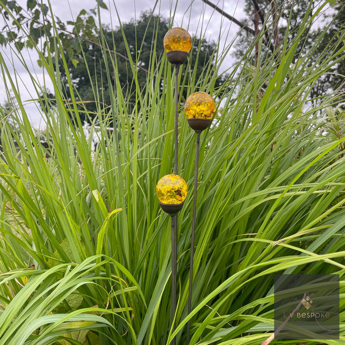 Glass Orb Cluster – amber orbs rising from green grassy foliage