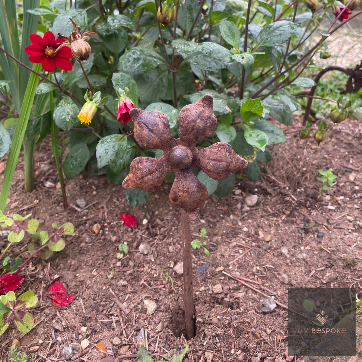Short floral metal garden stake – rust-brown metal flower in a bed of dahlias