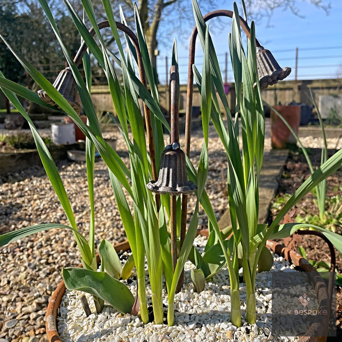 Short floral metal garden stakes – bell-flower stakes among green leaves in a gravel bed