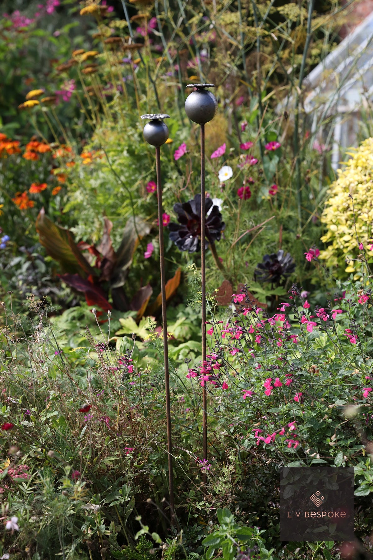 Tall floral metal garden stakes – small poppy seed heads with dark flowers in a border