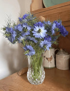 Blue and purple Nigella Miss Jekyll Mixed flowers in a faceted glass vase on a wooden worktop