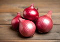 Onion Red Baron – four whole red onions on a rustic wooden surface