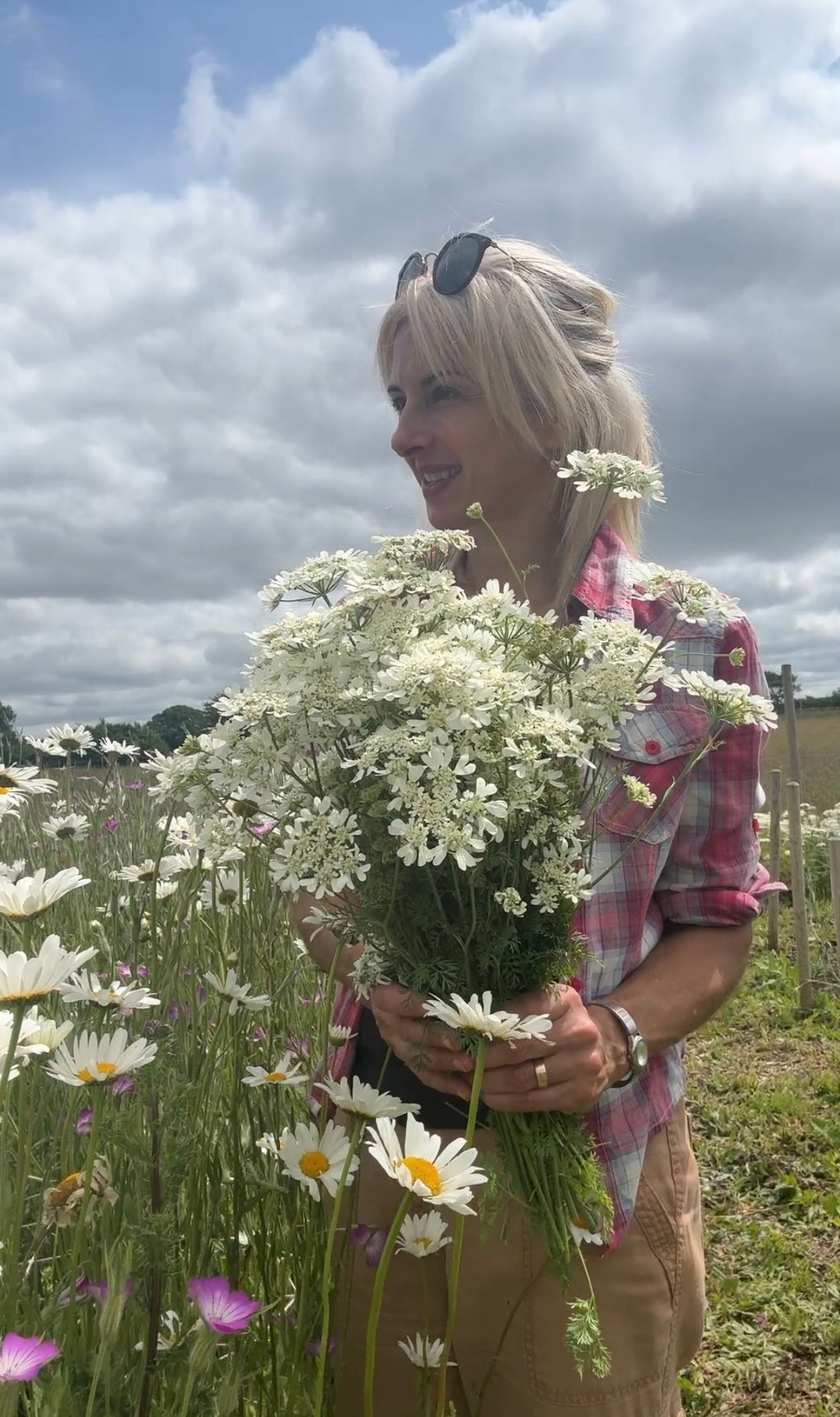 Woman carrying an armful of white Orlaya Grandiflora flowers in a field under a cloudy sky