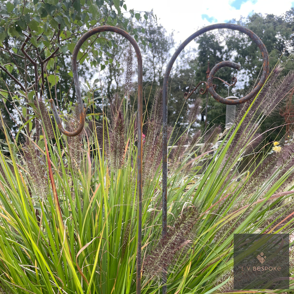Two scroll-top Shepherds Crook Hangers rising above ornamental grasses