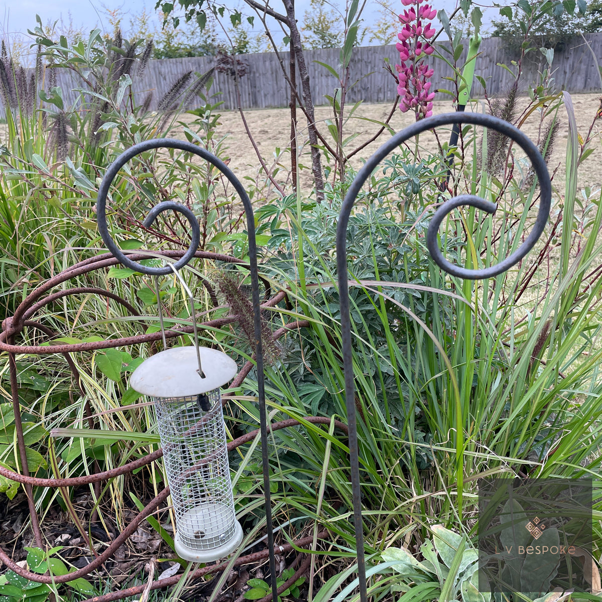 Scroll Shepherds Crook Hangers with a bird feeder hanging in a planted border