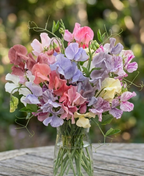 Sweet Pea Heaven Scent – pink, purple, white and cream blooms in a glass vase on a garden table