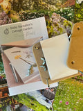 The Bishy Barnabees Cottage Garden Wooden Flower Press - Mini, complete with instructions and hardware, is shown atop colorful garden photos of blooming flowers and lush greenery.