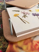 The Bishy Barnabees Cottage Garden Wooden Flower Press - Standard holds paper and flowers between wooden boards secured by metal bolts, with vibrant floral images peeking out, highlighting the beauty of flower pressing.